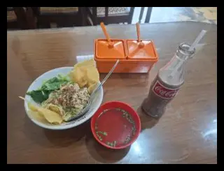 Closeup botol Es Fosco yang masih berembun bersanding dengan mangkuk Cwie Mie di atas meja kayu untu