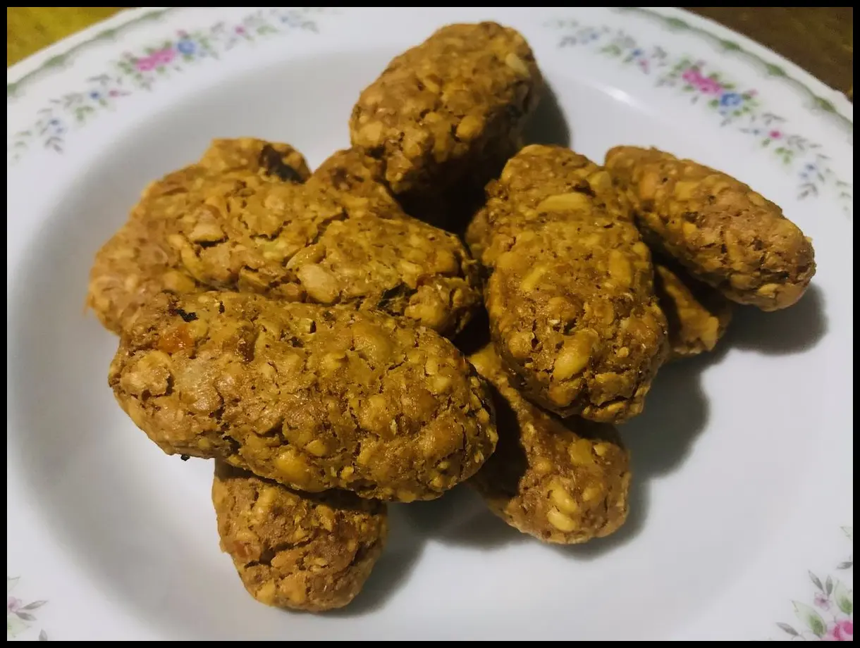 Piring berisi jajaran side dish seperti paru dan mendol yang tertata rapi di atas meja kayu panjang dengan latar belakang kepulan asap dari mangkuk rawon.