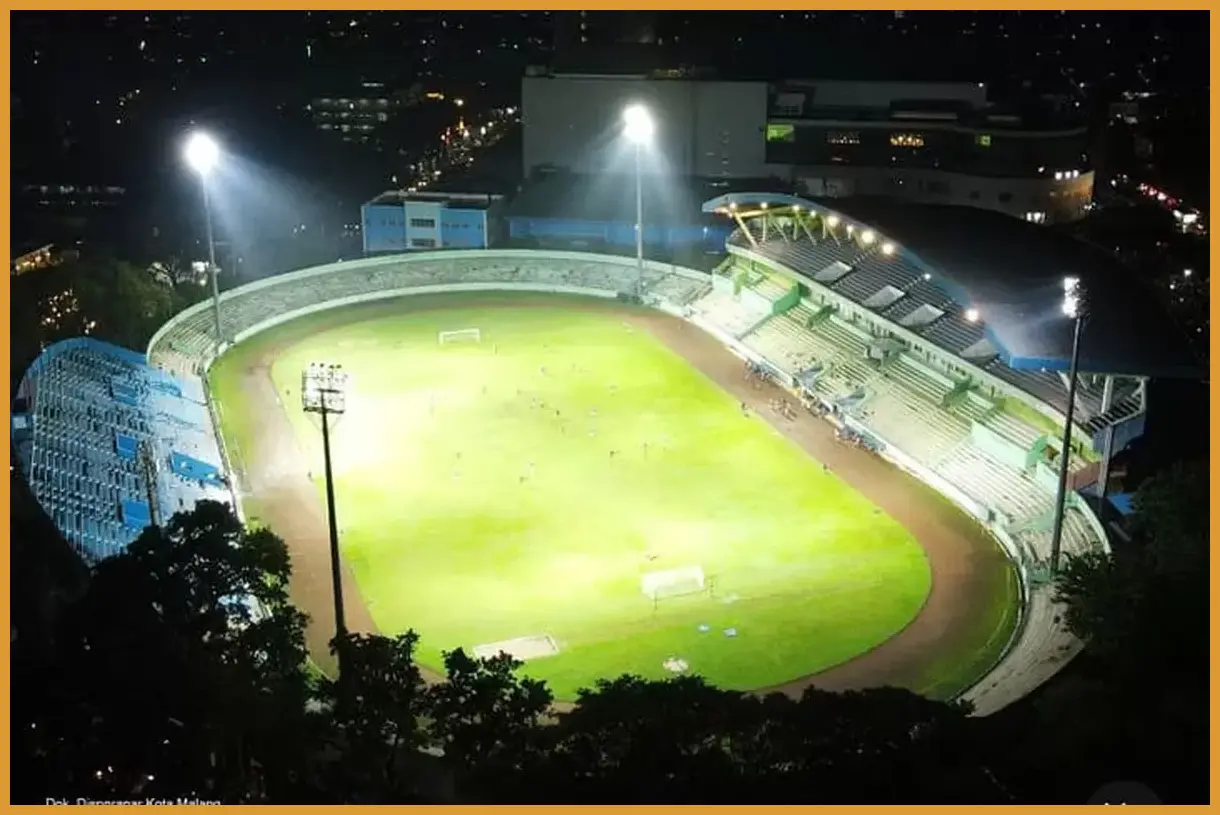 Ambil sudut pandang dari tribun VIP Stadion Gajayana saat lampu panggung menyala terang untuk menangkap lautan penonton dengan latar gedung-gedung kota.